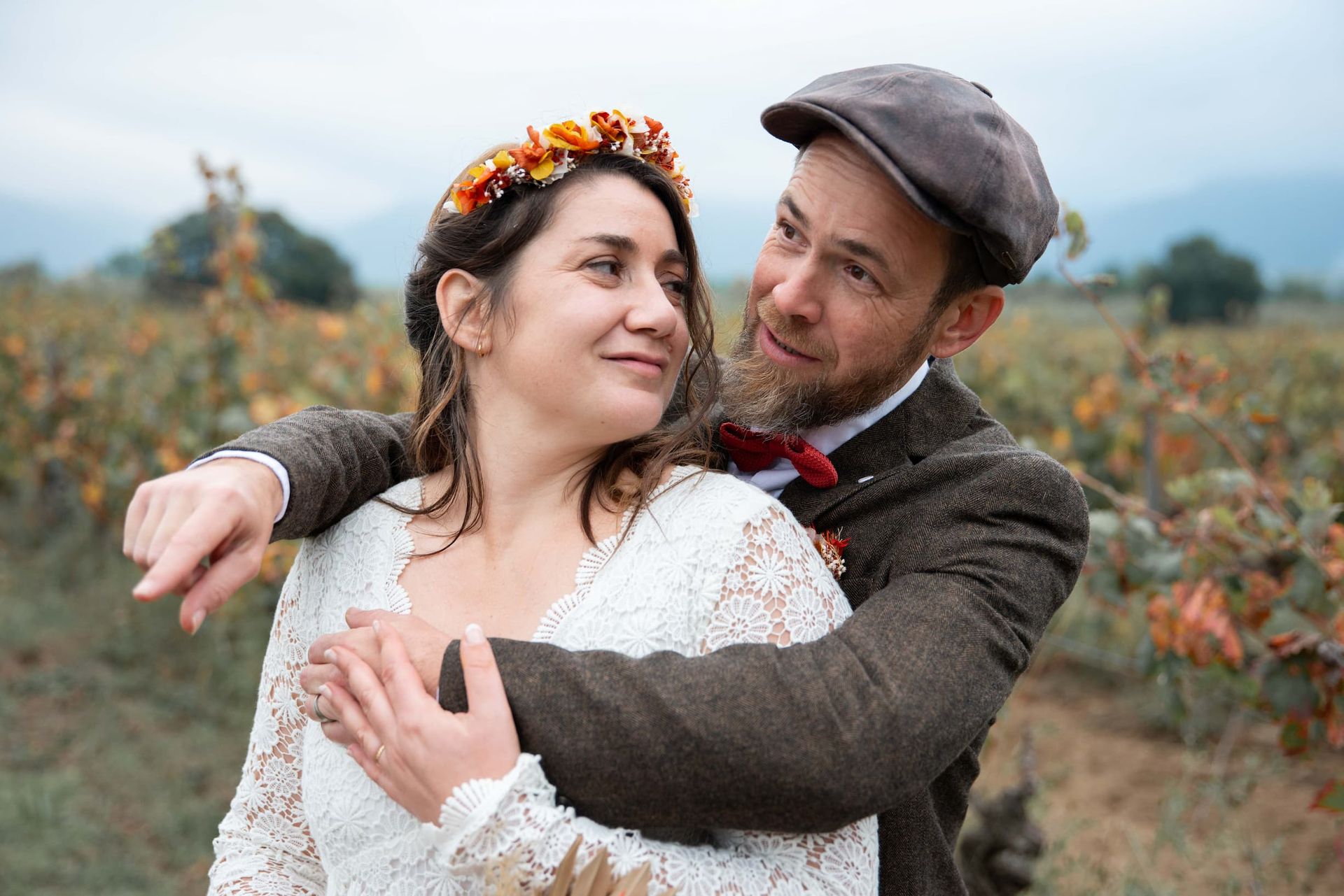Portrait des mariés enlacés dans les vignes en automne, couronne de fleurs orange et veste tweed — mariage champêtre Saint-Génis-des-Fontaines