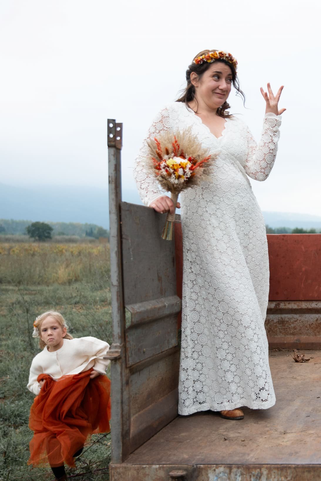 Mariée en robe dentelle et bouquet de fleurs séchées debout sur une remorque agricole, demoiselle d'honneur à ses pieds — Saint-Génis-des-Fontaines