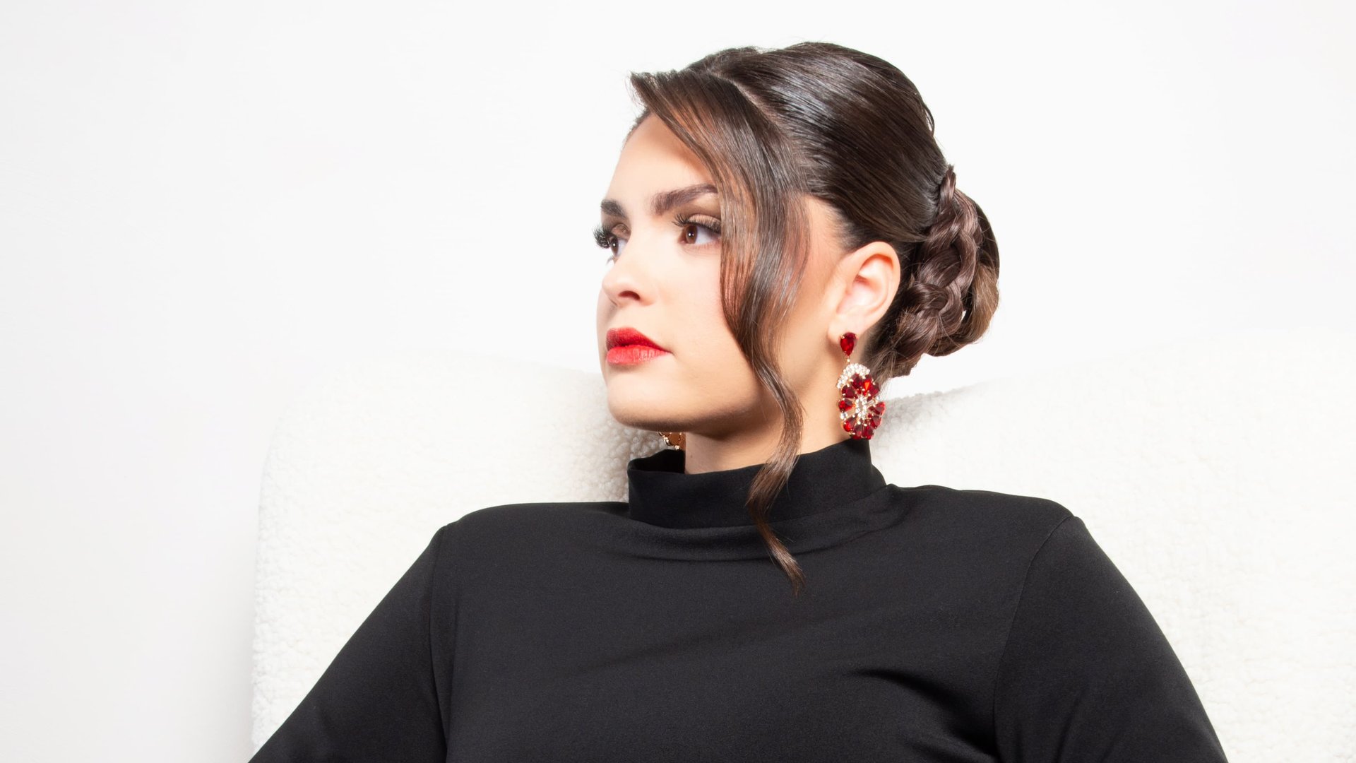 Portrait de modèle en col roulé noir, chignon tressé et boucles d'oreilles rouges — shooting inspiration mariage